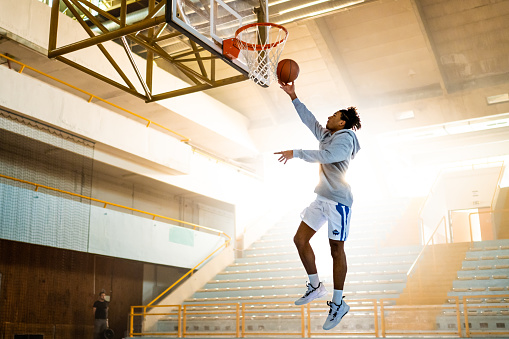 Basketball player throwing ball in hoop on sports court during practice.