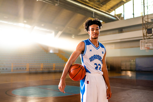 Portrait of basketball player standing while holding ball on sports court during practice.