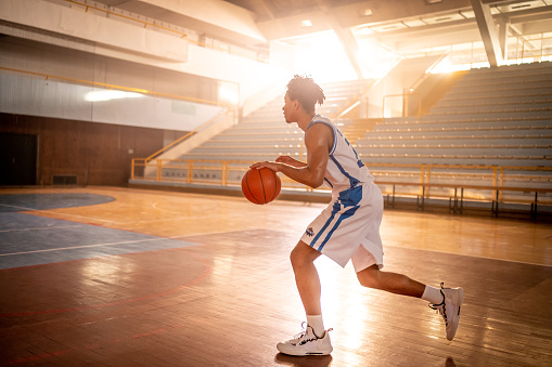 Basketball player dribbling while playing basketball alone on sports court during practice.