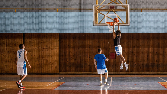 Male basketball player scoring slam dunk on court during practice.