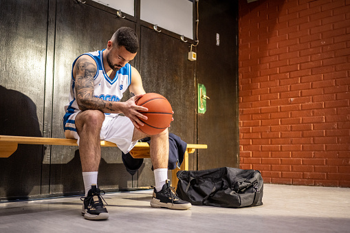 Young basketball player holding ball while sitting on bench in sports hall.
