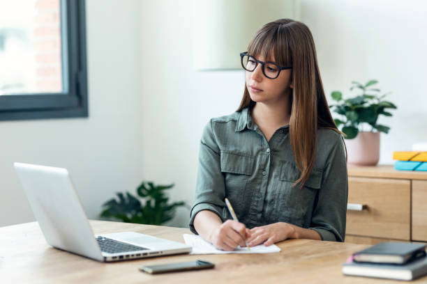 istock Concentrated young beautiful business woman working with laptop while taking some notes in the office. 1498635145