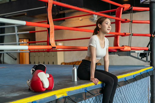 Asian female boxer taking a break in a boxing ring