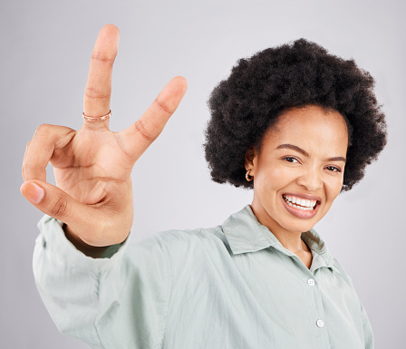 Portrait, peace sign and hand with a woman in studio on a gray background feeling happy or carefree. Smile, emoji and gesture with a happy young female indoor for freedom, wellness or good vibes