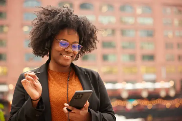 A tech-savvy professional, a businesswoman stands in Chicago downtown district, utilizing both her phone and a digital pen.