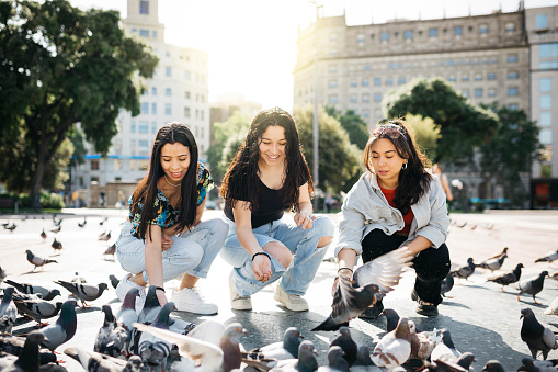 Three young women feeding pigeons in a square of Barcelona. Three friends enjoying a trip together.