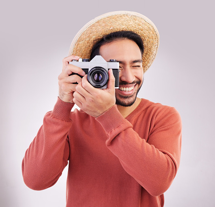Travel, camera and happy man on holiday, adventure and fun on white background. Smile, travel and person taking picture, photographer or tourist in studio for summer vacation, journey and happiness.