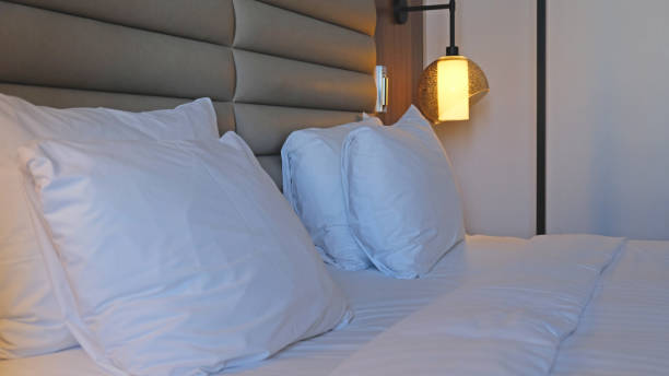 istock Close-up fragment of bedroom with empty bedside table, turn on reading lamp and a socket in modern interior​ design home or hotel. Soft pillow and blanket, stylish comfortable furniture. 1498644421