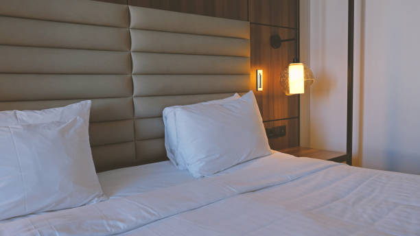 istock Close-up fragment of bedroom with empty bedside table, turn on reading lamp and a socket in modern interior​ design home or hotel. Soft pillow and blanket, stylish comfortable furniture. 1498644423