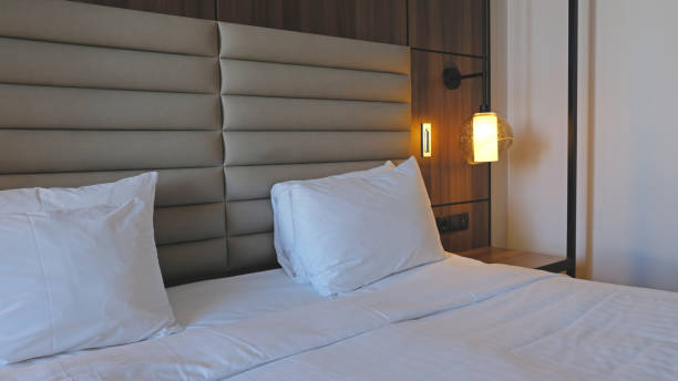 istock Close-up fragment of bedroom with empty bedside table, turn on reading lamp and a socket in modern interior​ design home or hotel. Soft pillow and blanket, stylish comfortable furniture. 1498644447