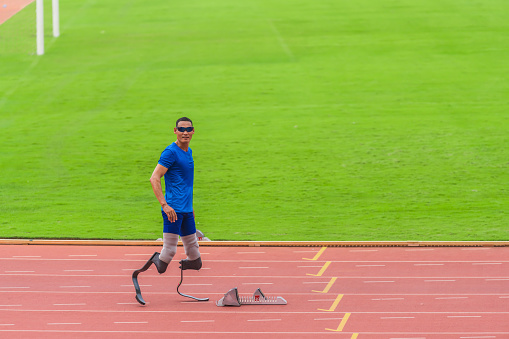 Asian athlete with prosthetics, poised at start block, primed for high-speed run on stadium track