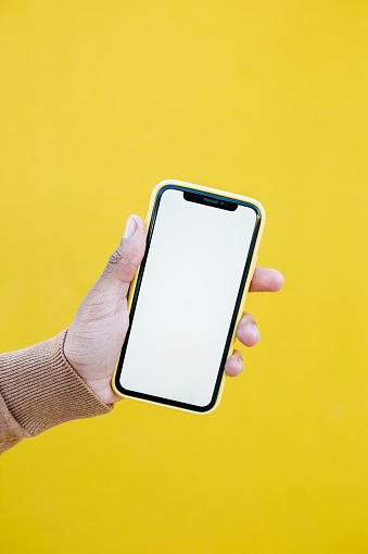 Human hand holding a yellow smartphone against a yellow background