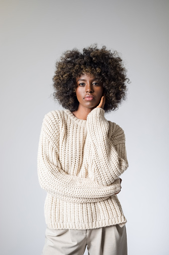 Portrait of young woman with afro hairstyle wearing white sweater and pants, looking at camera.