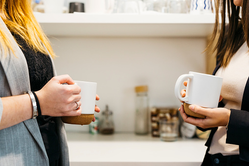 Close up of Two business woman's hands  holding a white mug, during a coffee break at the coffee area, in the office