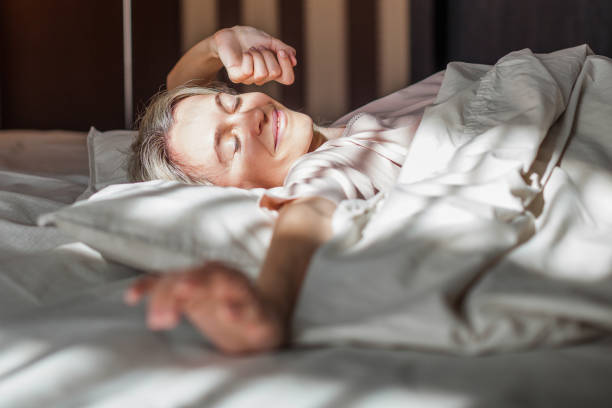 istock Happy middle aged woman sits on bed and stretching arms 1498649781