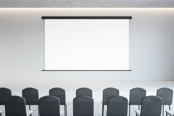 istock Front view on blank white poster with space for advertising text or logo on light wall background opposite black chair rows in lecture hall, seminar or marketing concept. 3D rendering, mock up 1498649838