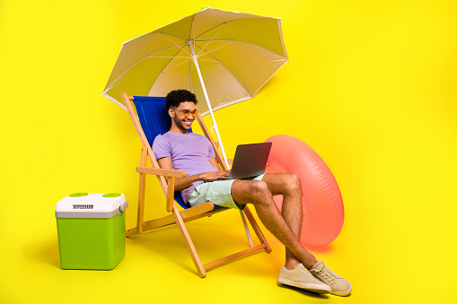 Full body cadre of young it specialist man using netbook lying sunbed satisfied his freelance job isolated on yellow color background.