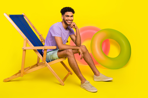 Full body photo of young man touch chin sitting concentrated sunbed posing for magazine travel agency isolated on yellow color background.