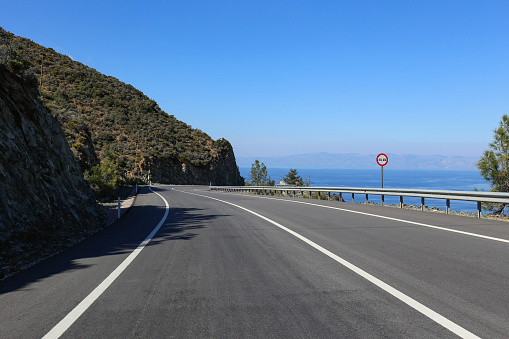 An empty mountain serpentine road with a beautiful sea view and no overtaking road sign. Copy space for text, background.
