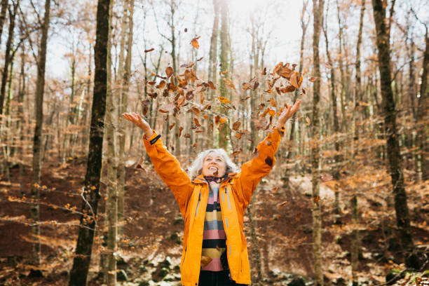 femme, dans une forêt, jetant des feuilles d’arbres d’automne en l’air - falling senior adult people one person photos et images de collection