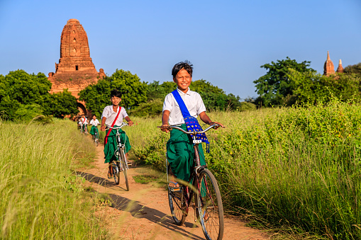 Young Burmese school children riding a bicycle, the ancient temples of Bagan on the background, Myanmar (Burma)