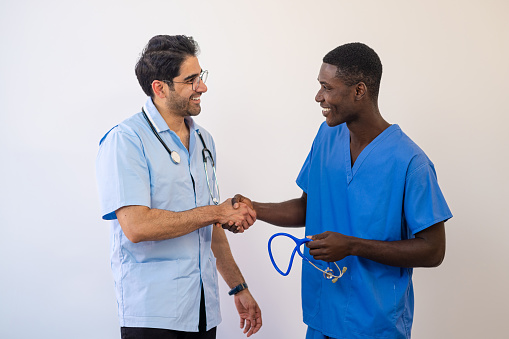 A front view of two men who work within the medicine industry in the UK. One is a nurse and the other is a doctor. They are both smiling and shaking each others hand. They work together in the same profession.