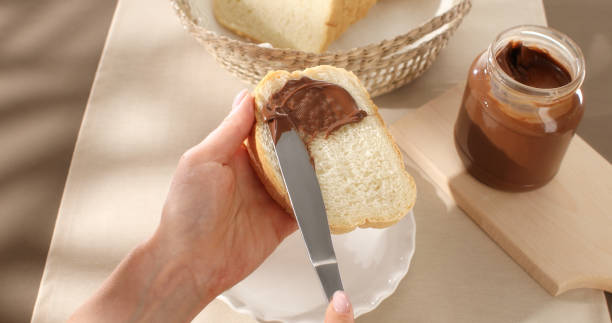 istock Female hands spreading chocolate butter on bread by knife. Angle view. 1498655513