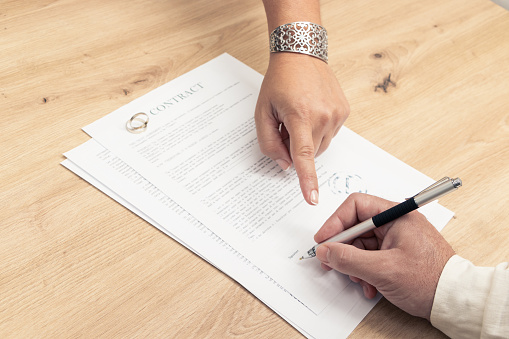 finger pointing to where to sign on some marriage contract papers with wedding rings on top of it