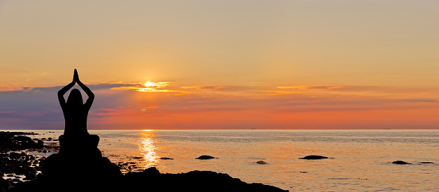 Silhouette of woman in yoga posture on beach at sunset