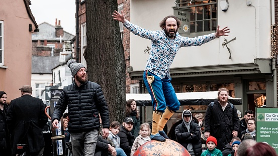 York, United Kingdom – February 11, 2023: A young man is balancing on an orange sphere, while a group of people watch in amazement