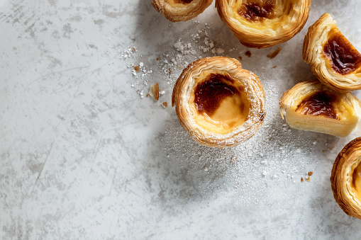 Crispy Portuguese custard tarts - Pasteis de nata, dusted with powdered sugar top view on grey surface
