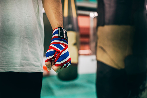 An Asian boxing enthusiast carefully wraps hand wraps around their palms before their boxing training, preparing for the upcoming training session.