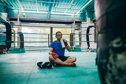 After completing a training session, an Asian boxer replenishes his fluids and takes a short rest to recover his energy. During this time, he reflects on the techniques he used during the training.