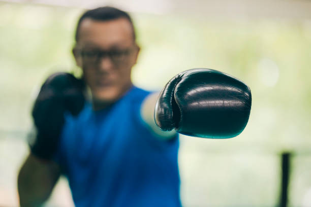 An Asian boxer stands on the ring, prepared for boxing action, with the camera focusing on his boxing gloves.