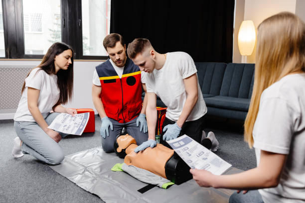 istock Young man instructor helping to make first aid heart compressions with dummy during the group training indoors 1498669565
