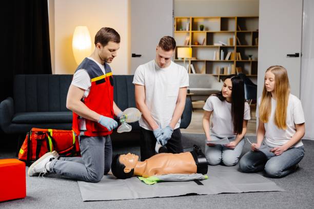 istock Young man instructor helping to make first aid heart compressions with dummy during the group training indoors 1498669566