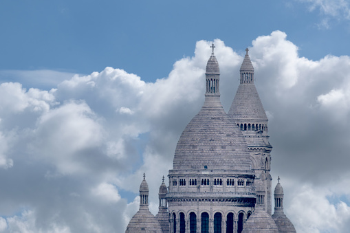 6 May 2023, Paris France. Telephoto shot of domes and turrets of Sacre Coeur Basilica in Paris showing details of stonework, ornamentation. Blue sky, clouds background