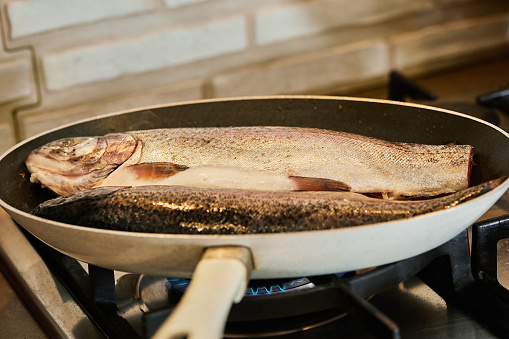 Trout is fried in pan on gas stove.