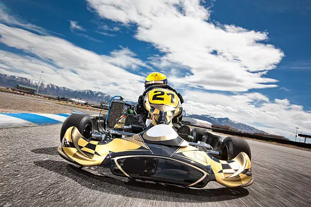 Front, low and wide angle view of a golden go-cart speeding along a race course under a cloudy sky. Motion blur in asphalt to emphasize speed.