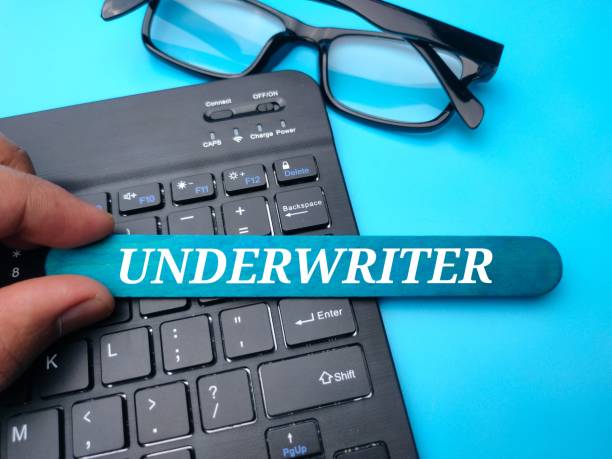 teclado y gafas con la palabra underwriter sobre fondo azul. - underwriting fotografías e imágenes de stock