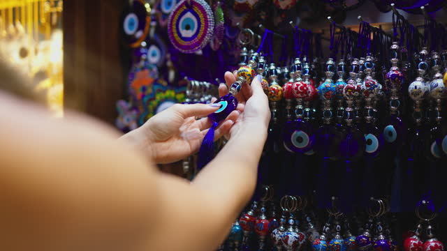 Young tourist woman examining evil eye beads in Istanbul Grand Bazaar, woman examining souvenirs in Istanbul, Talismans against the evil eye, Evil eye beads