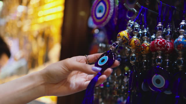 Young tourist woman examining evil eye beads in Istanbul Grand Bazaar, woman examining souvenirs in Istanbul, Talismans against the evil eye, Evil eye beads