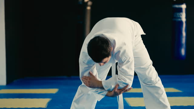 Young man in white kimono doing stretching exercises in martial arts school