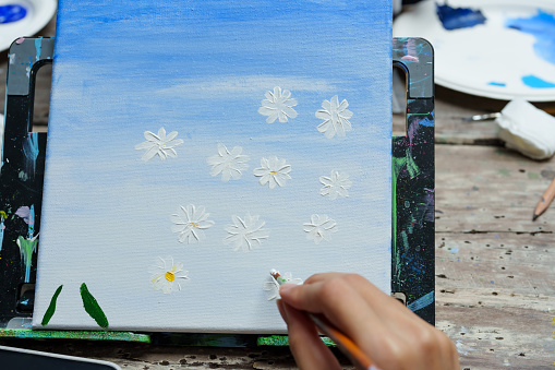Asian girls spend their free time on vacation. Use your hand to paint the paint brush on the fabric stretched on the wooden frame. Practicing drawing, making art work painting of flowers and sky