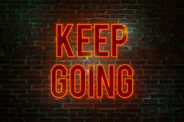 Brick wall at night with the text Keep Going in orange neon letters. The way forward, continuity, motivation, positive emotion, inspiration and encouragement. 3D illustration
