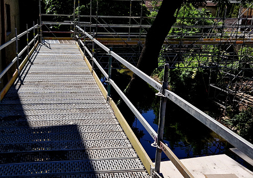 scaffolding surrounds the bridge, serving as a temporary footbridge. the bridge over the water from below must be repaired by masons from the platform. he quickly stands up and folds himself onto car, building construction, route change, transfer, under, workshop training, workspace, stonemason