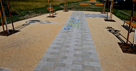 park promenade with paving with a maze pattern. games for children painted on the pavement with paint. blue and green circles. around it is a paved road the color of yellow compacted sand. open space, labyrinth, pavement