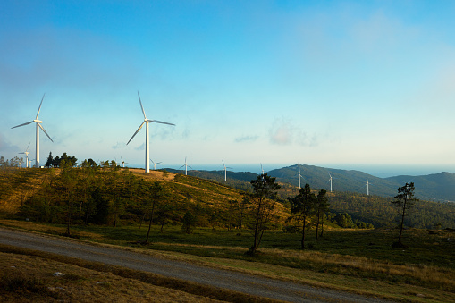Windmill farms in Northern Spain in landscape, near the sea with clouds moving into one section of the farm and others with clearer sky.