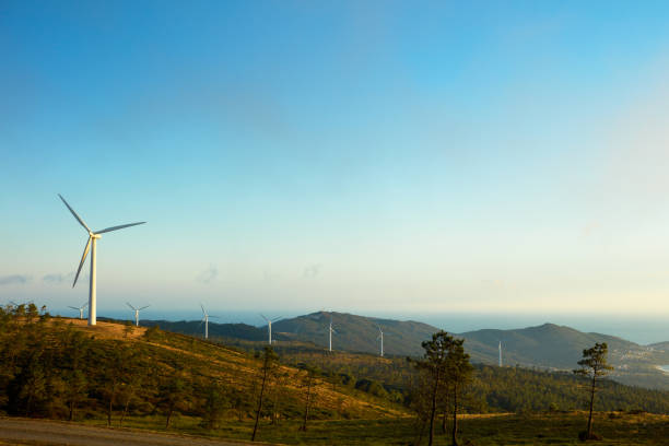 Windmill farms in Northern Spain in landscape, near the sea with clouds moving into one section of the farm and others with clearer sky.