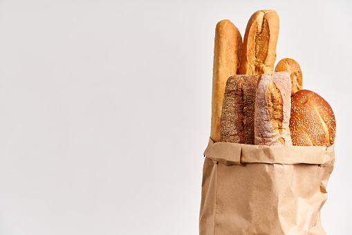 Different types of french bread baguettes in paper bag over white background with copy space. Bakery, delicious food concept